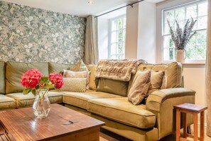 A living room with a sofa, a wooden coffee table, and a vase with flowers. - 3 Bed in Baslow (oc-t44870) (Baslow)