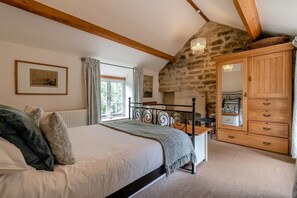 A bedroom with a bed, a dresser, a window with curtains, a stone wall, and a chandelier. - 3 Bed in Baslow (oc-t44870) (Baslow)