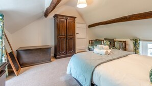 Een slaapkamer met een schuine kap, een grote kast, een bed met opgerolde handdoeken en een raam met gordijnen.