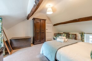 Ein Schlafzimmer mit schrägverdeckter Decke, einem großen Kleiderschrank, einem Bett mit zusammengerollten Handtüchern und einem mit Vorhängen versehenen Fenster.