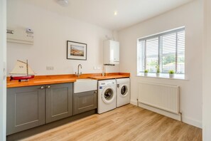 Eine moderne Küche mit grauen Schränken, einer Holz Arbeitsplatte, einer Waschmaschine und einem Fenster mit Jalousien.