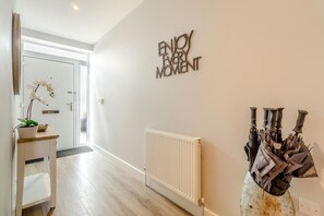 Ein Flur mit einer weißen Tür, einem Heizkörper und einem an der Wand befestigten Schild mit der Aufschrift 'ENJOY EVERY MOMENT'.