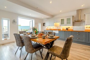 Een moderne keuken met grijze kastjes, een houten eettafel en uitzicht naar buiten.