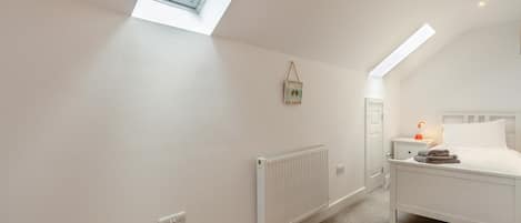A bedroom with a skylight, a radiator, a bedside table with a lamp, and a bed with pillows.
