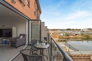 Een balkon met een glazen deur, een grijze bank en een tafel met wijnglazen.