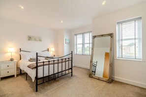 Ein Schlafzimmer mit einem Bett, Nachttischen, einem Spiegel und Fenstern.
