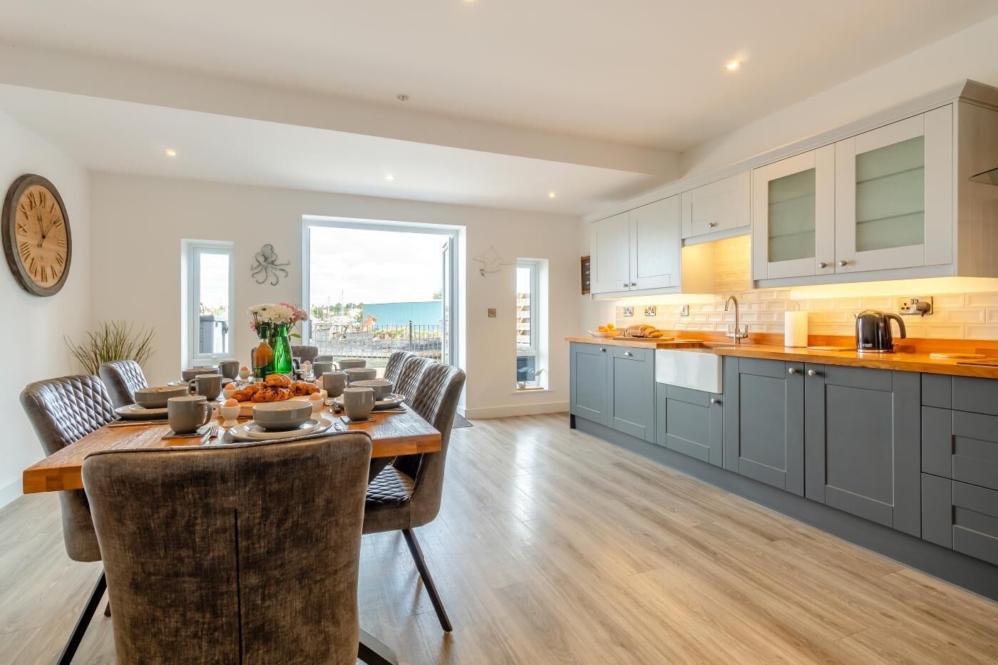 A modern kitchen with grey cabinets, a wooden countertop, and a view to the outside.