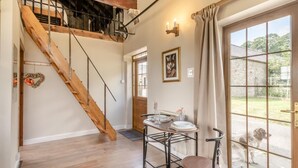 A room with a wooden staircase, a dining area with a table and chairs, and a view through a glass door. - 1 Bed in Gilsland (oc-j45730) (Waterhead)