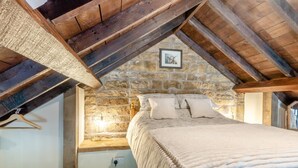 A bedroom with a stone wall, a bed with pillows, a hanging light fixture, and a wooden ceiling. - 1 Bed in Gilsland (oc-j45730) (Waterhead)