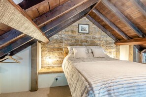 Ein Schlafzimmer mit Steinsturz, einem Bett mit Kissen, einer hängenden Leuchte und einer Holzzahl.