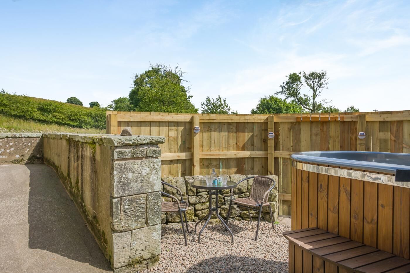 Een terras buiten met een jacuzzi, een stenen muur en een houten omheining.