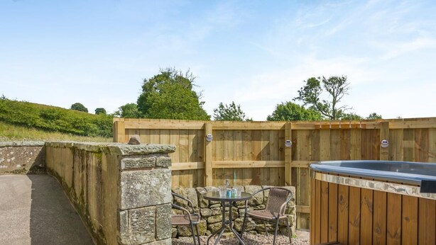 An outdoor patio with a hot tub, stone wall, and wooden fence. - 1 Bed in Gilsland (oc-j45730) (Waterhead)