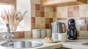 A kitchen with a stainless steel sink, a coffee maker, a croissant on a plate, and a vase with dried flowers. - 1 Bed in Gilsland (oc-j45730) (Waterhead)