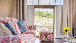 A living room with a floral sofa, a matching ottoman, and a vase with a sunflower. - 1 Bed in Gilsland (oc-j45730) (Waterhead)