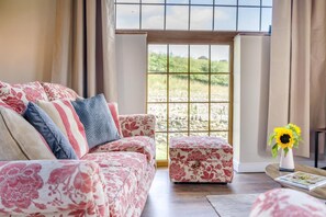 Ein Wohnzimmer mit einem blumigen Sofa, einem passenden Hocker und einer Vase mit einem Sonnenblume.