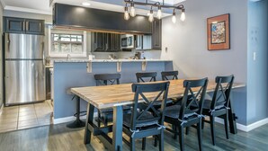 Una cocina moderna con un refrigerador de acero inoxidable, un microondas y un comedor con una mesa de madera y sillas negras.