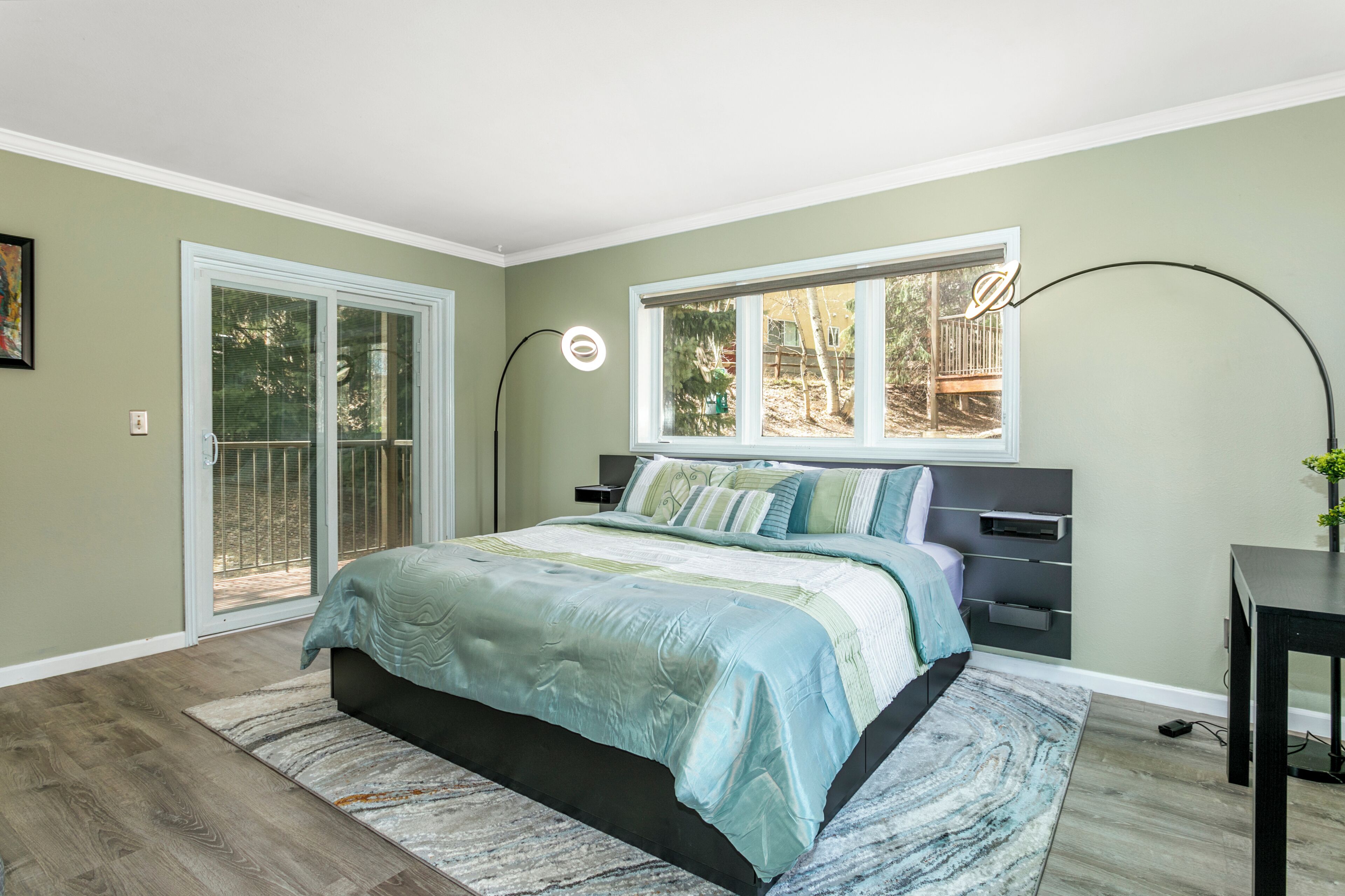 A bedroom with a bed, a nightstand, a desk, a window, and a door.