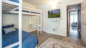 Una habitación con literas, un televisor montado en la pared y una puerta que da a otra habitación.