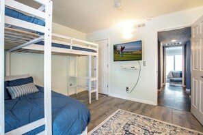 Ein Zimmer mit Etagenbetten, einem an der Wand befestigten Fernseher und einer Tür zu einem anderen Raum.