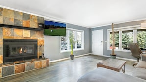 Una sala moderna con chimenea de piedra, un televisor de pantalla plana montado encima y un ventanal que ofrece vistas al exterior.