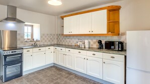 Una cocina moderna con gabinetes blancos, una campana de acero inoxidable, un horno integrado y una cafetera sobre la encimera.