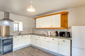 A modern kitchen with white cabinets, a stainless steel range hood, a built-in oven, and a coffee maker on the countertop. - 2 Bed in Gilsland (oc-o45731) (Waterhead)