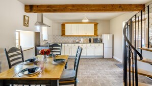 Un comedor con una mesa y sillas de madera, una cocina al fondo y una escalera en espiral.