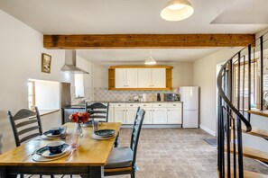 A dining area with a wooden table and chairs, a kitchen in the background, and a spiral staircase. - 2 Bed in Gilsland (oc-o45731) (Waterhead)