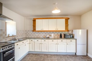 Een keuken met witte kastjes, een inbouwoven, een koelkast en een magnetron.