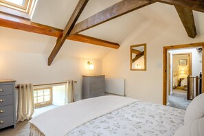 Een slaapkamer met een schuine balklaag, een bed met een bloemenprintdeken, een dressoir, een spiegel en een radiator.