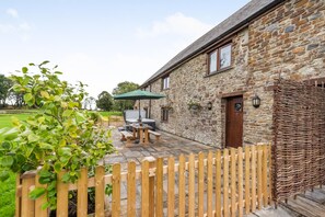 A stone building with a wooden fence, a patio with a table and chairs, and a green umbrella. - 2 Bed in St. Giles (oc-c45183) (Saint Giles in the Wood)
