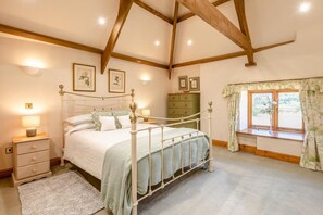 A bedroom with a four-poster bed, a nightstand with a lamp, a dresser, and a window with curtains. - 2 Bed in St. Giles (oc-c45183) (Saint Giles in the Wood)