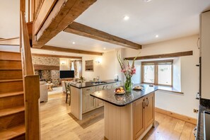 A spacious kitchen with a central island, wooden beams, a stone fireplace, and a large window. - 2 Bed in St. Giles (oc-c45183) (Saint Giles in the Wood)