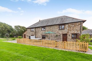 A stone house with a fenced yard, a swing set, and a green umbrella. - 2 Bed in St. Giles (oc-c45183) (Saint Giles in the Wood)