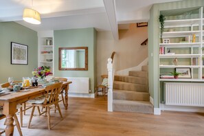 Ein Essbereich mit Holztisch und -stühlen, einer Treppe und einem Bücherregal mit unterschiedlichen Gegenständen.