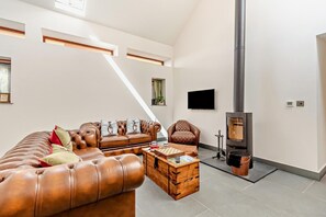 A spacious living room with a leather sofa, a wooden coffee table, a fireplace, and a television mounted on the wall. - 3 Bed in Challacombe (oc-s45342) (Challacombe)