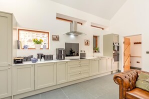 A modern kitchen with a central island, built-in appliances, and a dining area with a leather sofa. - 3 Bed in Challacombe (oc-s45342) (Challacombe)
