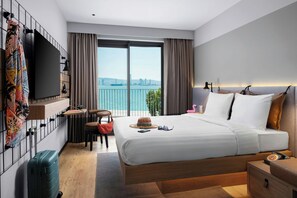 Habitación de hotel con una cama grande, un escritorio, una silla, un televisor y vistas a la ciudad por la ventana.