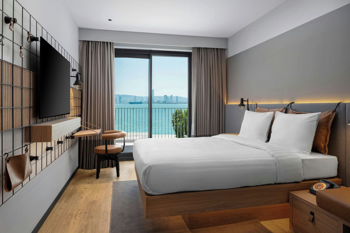 Habitación de hotel moderna con una cama grande, un escritorio, una silla, un televisor y vistas al agua.