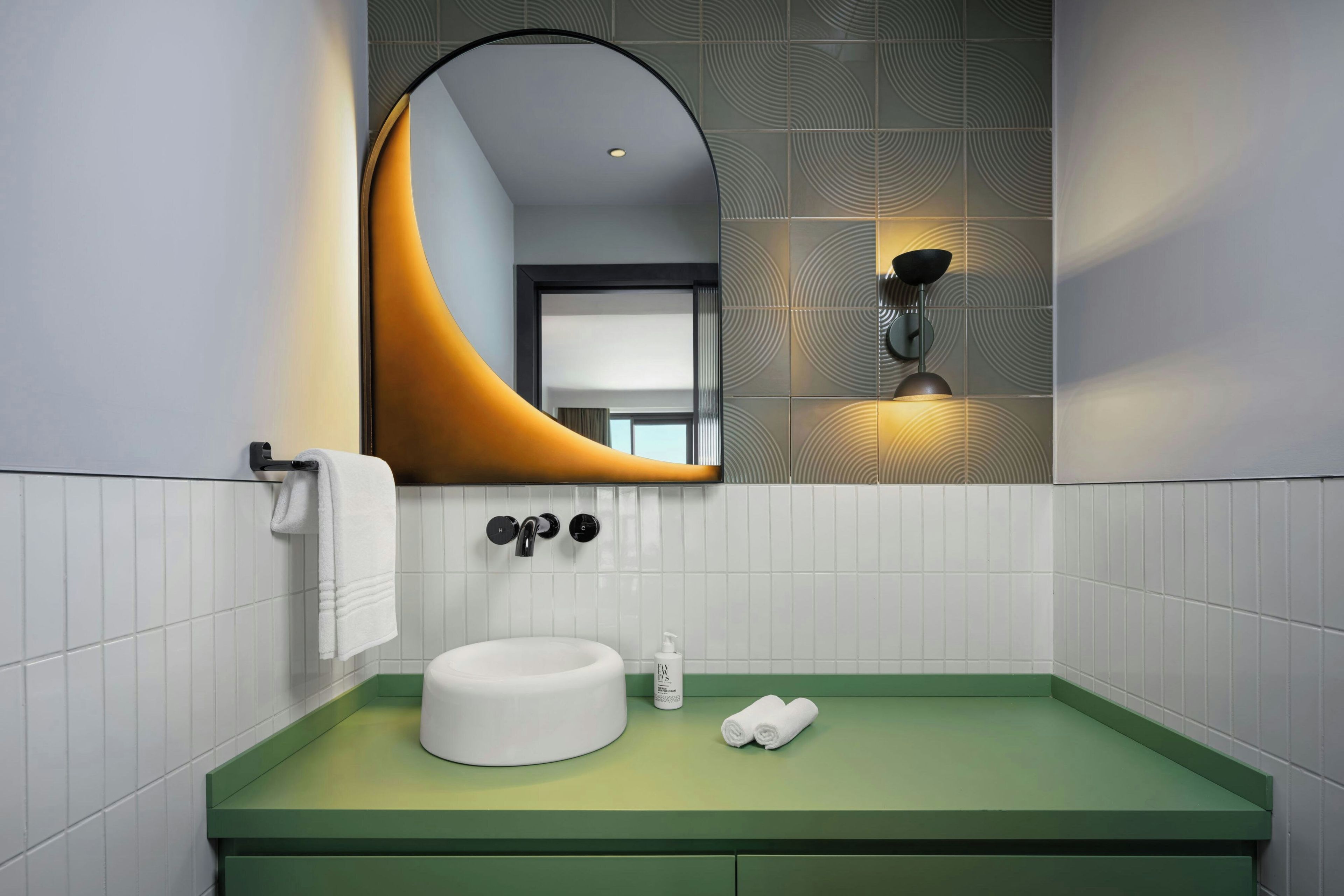 Une salle de bain moderne avec un meuble-lavabo vert, un lavabo blanc, un miroir rond et un porte-serviettes.