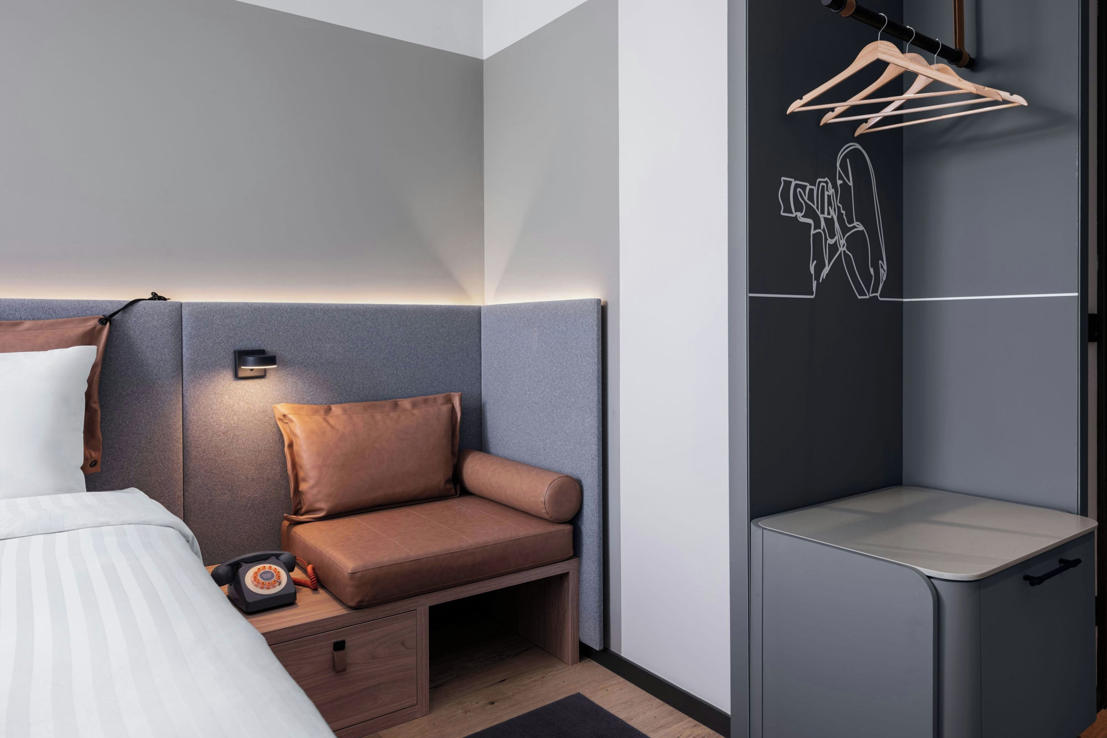 A modern hotel room with a bed, a seating area, a small wooden cabinet, and a wall-mounted drying rack.