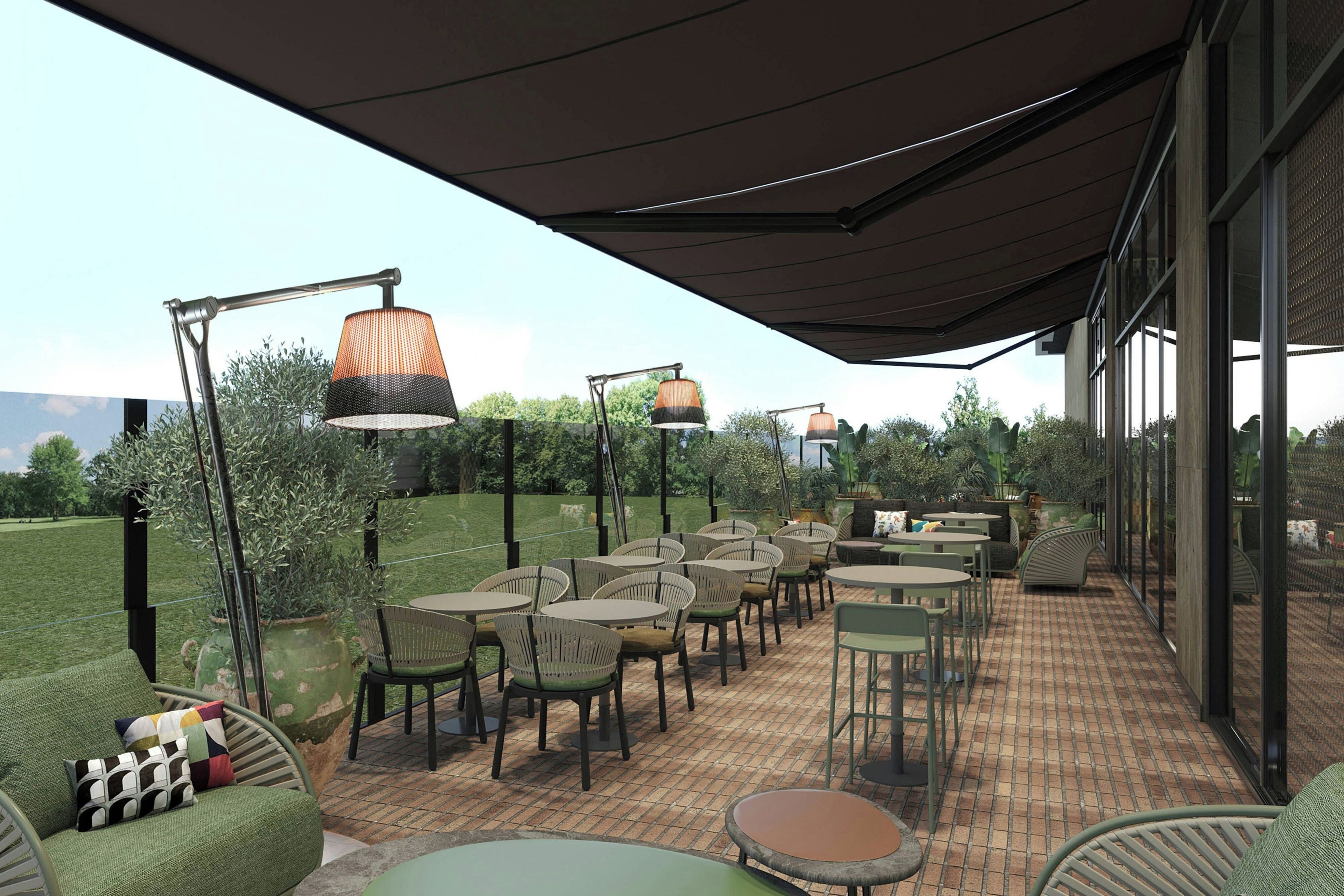 An outdoor patio with tables and chairs, a covered area with hanging lamps, and a view of greenery in the background.