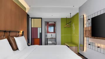Habitación de hotel con una cama grande, un armario, un espejo, un televisor y un baño visible a través de una puerta abierta.