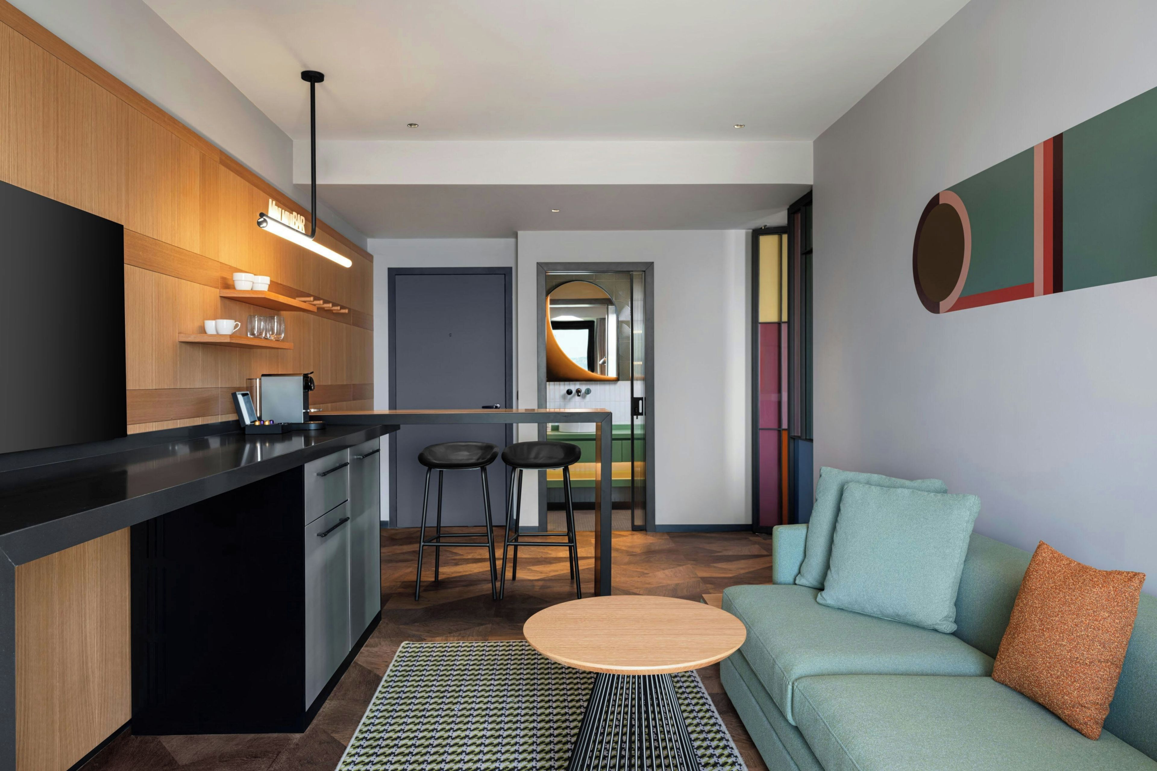 A modern kitchen with a bar area, a dining space with stools, and a living area with a sofa and cushions.