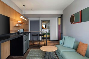 Cocina moderna con barra, zona de comedor con taburetes y sala de estar con sofá y cojines.