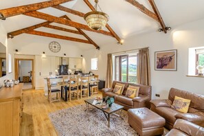 A spacious living area with a high ceiling, wooden beams, a dining table, leather sofas, and a view of the outdoors. - 3 Bed in Tremar Coombe (oc-g45783) (Tremar)