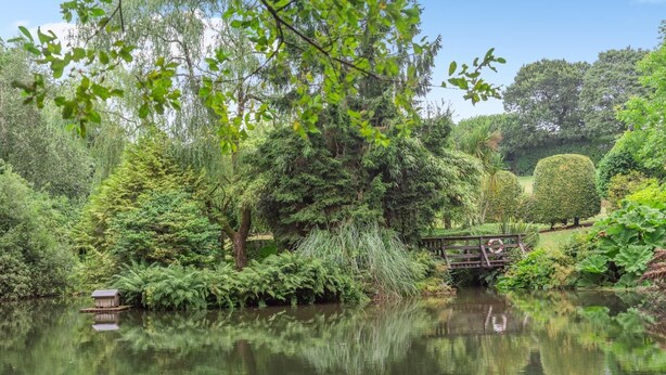 A tranquil garden with a pond, lush greenery, and a wooden bridge. - 3 Bed in Tremar Coombe (oc-g45783) (Tremar)