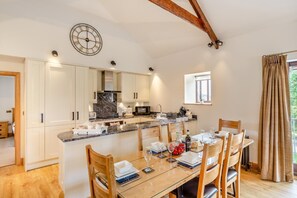 A modern kitchen with white cabinets, a marble countertop, and a dining area with wooden chairs and a glass table. - 3 Bed in Tremar Coombe (oc-g45783) (Tremar)