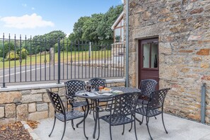 Eine Terrasse im Freien mit einer Steinmauer, einem Metallzaun und einem Tisch mit Stühlen.