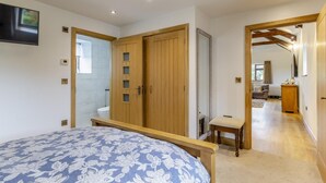 A bedroom with a bed, wooden wardrobe, and a small bench. - 3 Bed in Tremar Coombe (oc-g45783) (Tremar)